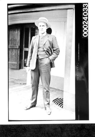 Man standing on deck wearing a a suit and boater and holding papers