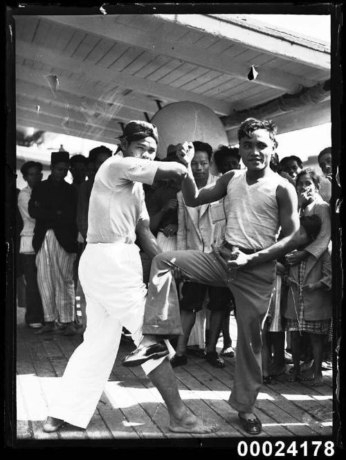 Two men with arms and legs raised in combat pose on SS VAN REES