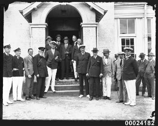 Men in civilian and maritime dress standing outside the entrance to the Royal Sydney Yacht Squadron building