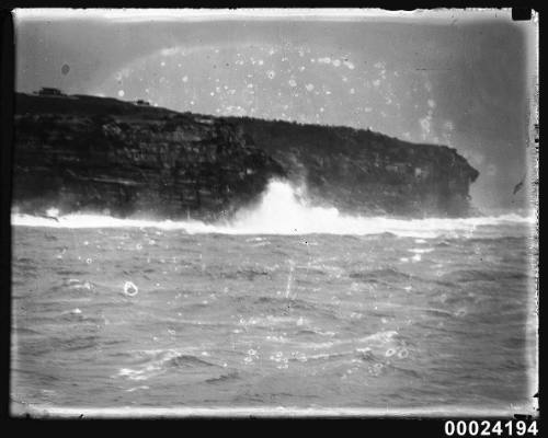 Waves breaking against a cliff face, viewed from the sea