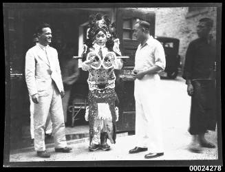 Image of a Japanese man in elaborate costume flanked by two men in an urban setting possibly in Nagoya, Japan
