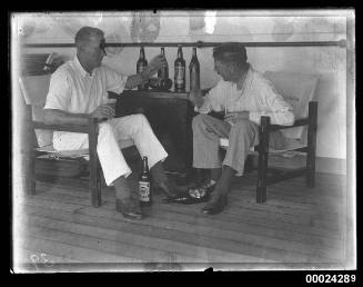 Two men seated, drinking beer and smoking cigars on board SS TANDA