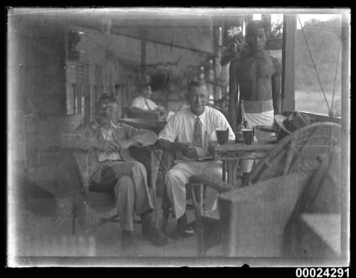 Image of two men seated with a man standing beside them possibly on board SS TANDA