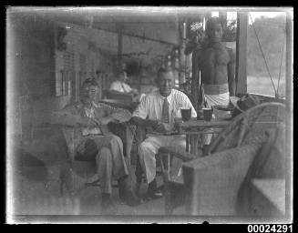 Image of two men seated with a man standing beside them possibly on board SS TANDA