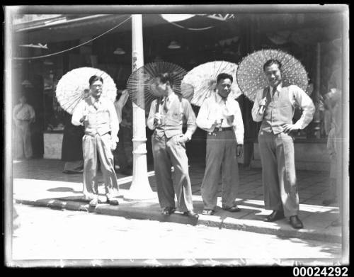 Four Japanese men wearing suits and holding parasols by a roadside possibly in Nagoya, Japan