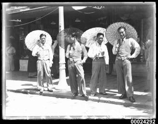 Four Japanese men wearing suits and holding parasols by a roadside possibly in Nagoya, Japan