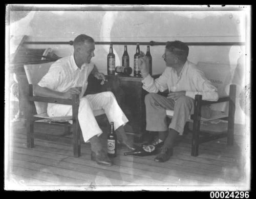 Two men seated, drinking beer and smoking cigars on board SS TANDA