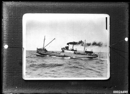 Single-funnel, two-masted merchant vessel under steam in a harbour