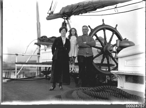 Ship's captain, wife and daughter standing at ship's wheel