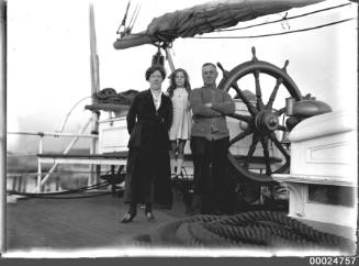 Ship's captain, wife and daughter standing at ship's wheel