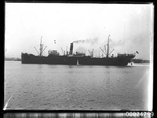 View of unidentified single funnel two masted cargo ship under way in harbour.