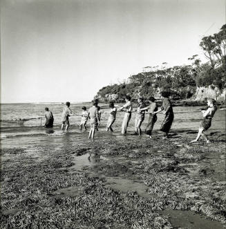 Photograph of men and children hauling a net onto a beach