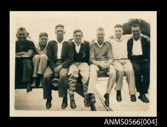 Photograph depicting seven men sitting on a diving board