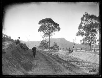 Two men standing by the side of a dirt road