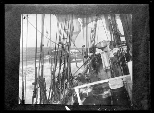 Three crewman rail hauling on a rope at the starboard rail of a sailing ship