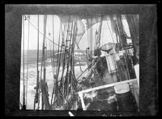 Three crewman rail hauling on a rope at the starboard rail of a sailing ship