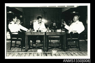 Captain Dun seated at table with two men