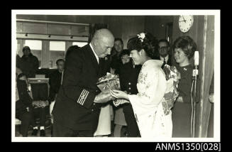 Captain Dun being presented with a gift from a woman dressed in a kimono