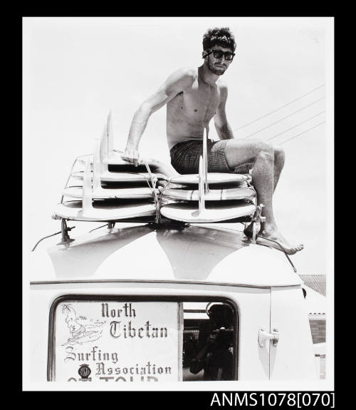 Man sitting on a surfboards on top of a car