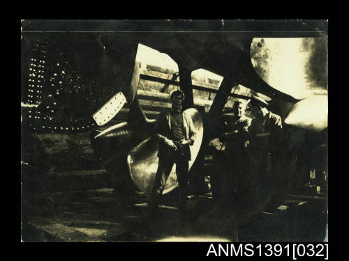 Photograph depicting three men posing next to two ship's propellers