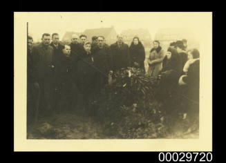 A group of people standing around a mound with funeral wreaths