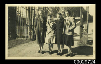 Four young women standing outside a wooden gate
