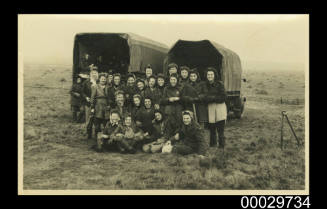 A group of people standing in front of two army trucks
