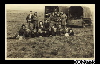 Young women posing in front of two army trucks