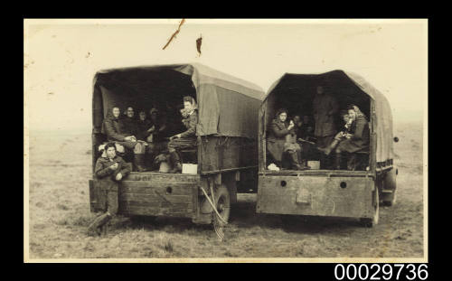 Young women seated in two army trucks