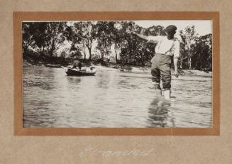 Man walking in river, pants rolled up, water half way up calves