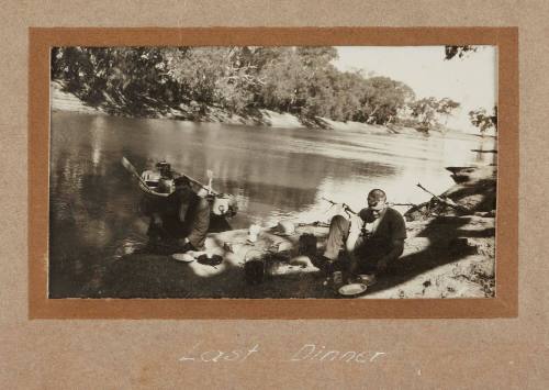 Two men eating picnic sitting on a river bank