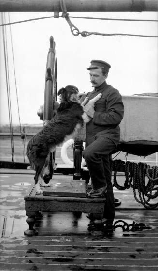 Ship's officer with pet dog, posed at ship's wheel