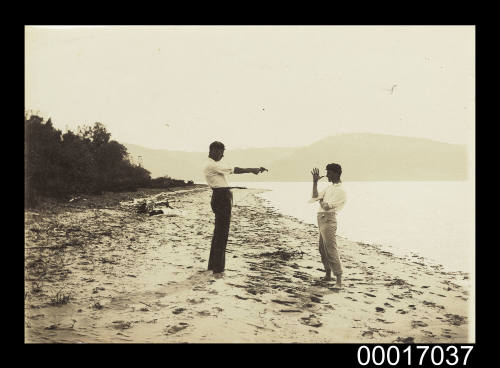 Two men play acting on a beach with a pistol