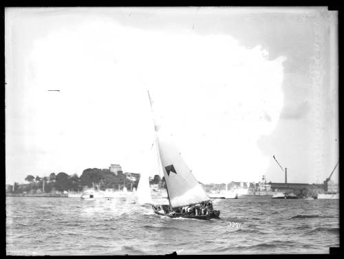 Gaff rigged skiff with quartered rectangle sail insignia sailing near Garden Island on Sydney Harbour