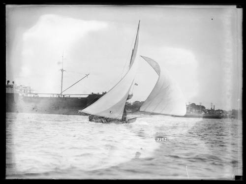 Large gaff rigged yacht  sailing before the wind on Sydney Harbour, freighter in background