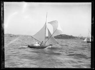 Small Gaff-rigged dingy with 3 crew visible passes Garden Island on Sydney Harbour.