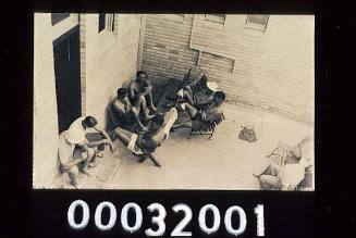 SEPIA TONED POSTCARD WITH MEN SITTING ON BENCH CHAIRS IN A COURTYARD, PROBABLY MEMBERS OF THE QUEENSCLIFF SURF LIFE SAVING CLUB