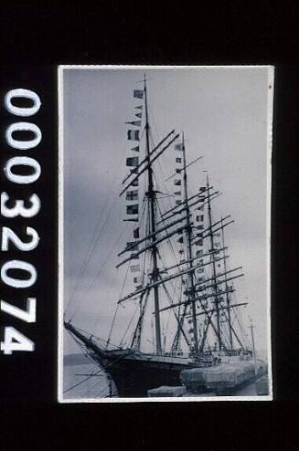 Four master barque KOMMODORE JOHNSEN, ex MAGDALENE VINNEN moored to a wharf and with communication flags down each mast 