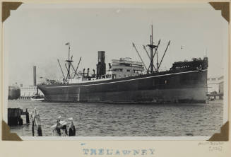 Photograph of  TRELAWNY depicting bow and starboard side of cargo ship at anchor in port with wharf buildings off port side