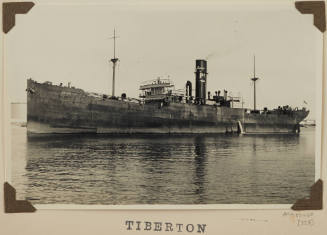 Photograph  TIBERTON depicting port side of  cargo ship off buildings on shore in distance on starboard side