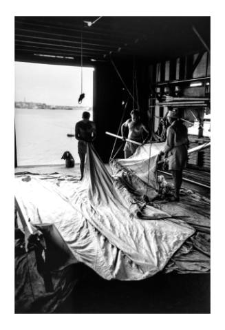 Three men preparing 18-foot skiff sails in a boatshed