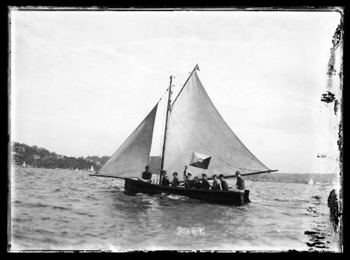 Gaff-rigged large skiff with nine crew, skiff has oblong sail insignia in coloured quarters