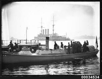 Japanese sailors standing on board a steam pinnace with HIJMS IZUMO in the background