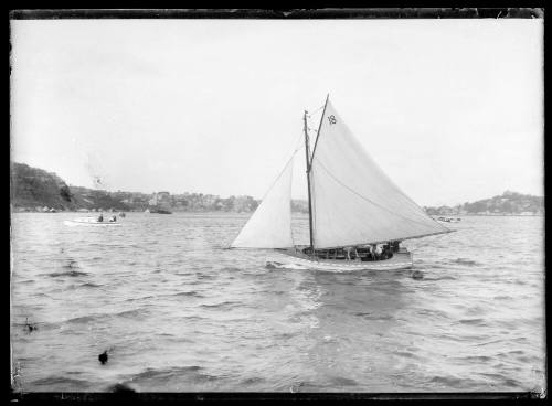 Gaff-rigged open yacht with four crew bailing out cockpit