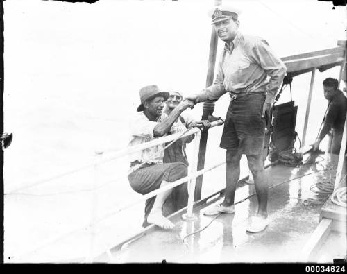 Civilians climbing aboard a vessel with an officer lending a hand