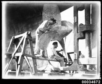 Two sailors cleaning a propeller of the French warship BELLATRIX