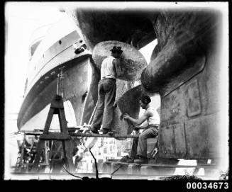 Two sailors cleaning a propeller of the French warship BELLATRIX