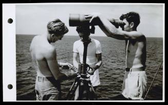 A16731 - A.B. Tanner, RAN, from Melbourne, and A.B. Walters, RAN, from Colac, Victoria, and Tel. Fisher, RAN, from Brisbane, inspecting a large pair of Japanese binoculars now in possession of the ship's crew of HMAS GLENELG