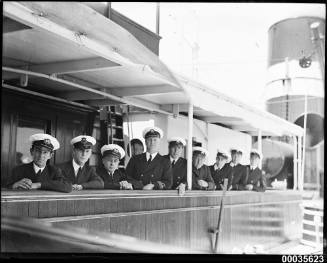 Captain and officers leaning on a wooden railing