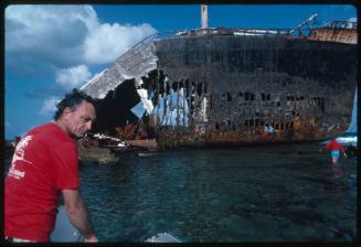 Ron Taylor in front of a large corroded shipwrecked vessel